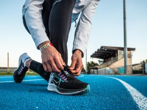 Zoom sur les pieds d'un homme faisant ses lacets, avec une paire de Nike Zoom Pegasus 38 au pied. Il est sur une piste d'athlétisme en tartan bleu. Il y a une tribune de stade en arrière plan.
