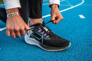 Zoom sur les pieds d'un homme faisant ses lacets, avec une paire de Nike Zoom Pegasus 38 au pied. Il est sur une piste d'athlétisme en tartan bleu.