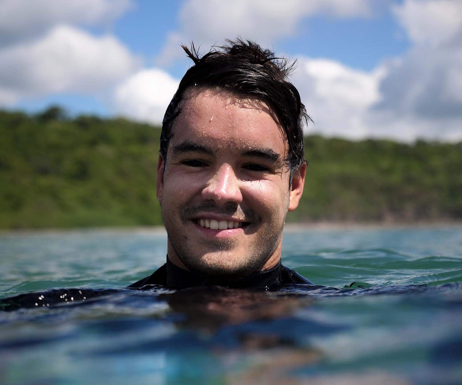 Portrait de Robin Aussenac, en combinaison de surf, avec seulement la tête dépassant au dessus de la surface de l'eau lors d'un tournage aquatique