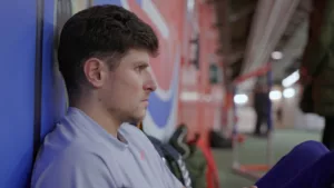 Plan rapproché sur le visage de Benjamin Robert, assis contre le mur du stade d'échauffement de l'Arena Stade Couvert de Liévin, avant sa course au Meeting de Liévin