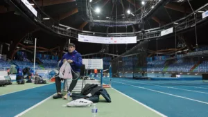 Plan large de Benjamin Robert, assis sur une chaise au milieu de l'Arena Stade Couvert de Liévin, avant de mettre ses chaussures pour s'entrainer la veille du Meeting de Liévin.